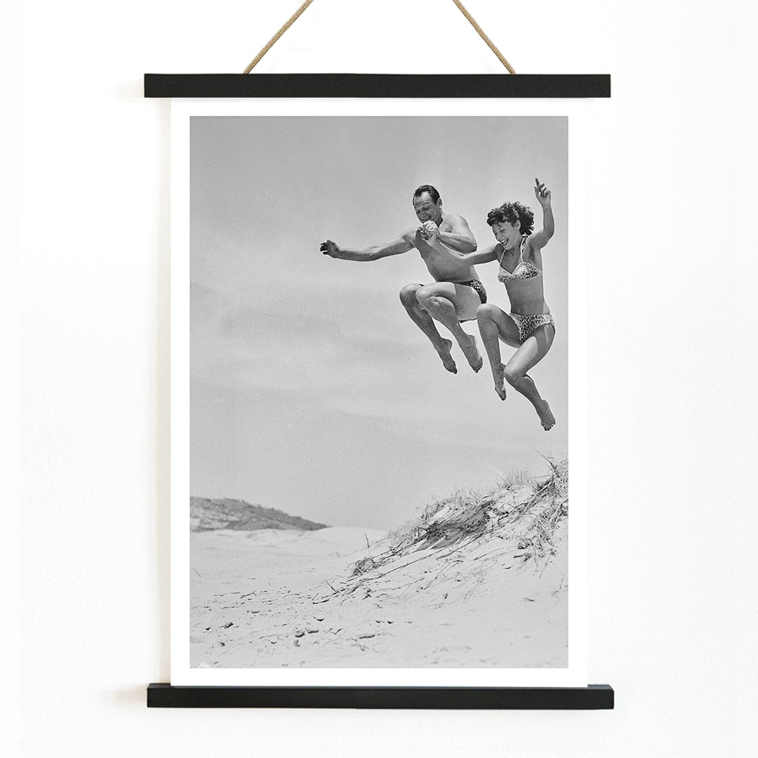 Two Tivoli Stars performing an acrobatic jump on a sandy beach in swimsuits Acrobatics at the Beach poster, with wooden magnetic frame on white background