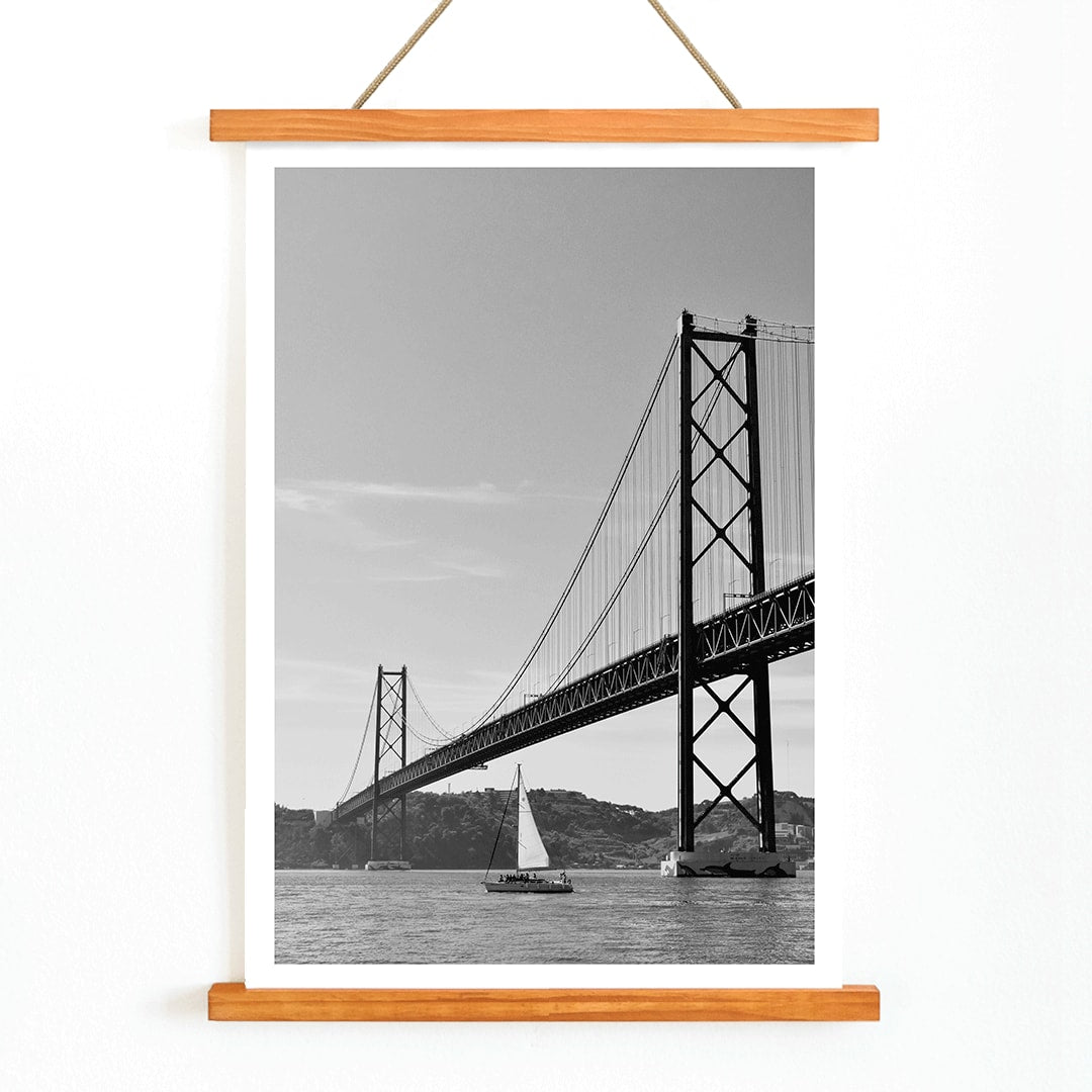 Lisbon Bridge Black and White Poster by Raphael Alves featuring a framed photograph of a suspension bridge and sailboat in the water, with wooden magnetic frame on white background