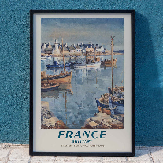 France Brittany Railway poster by Edmond Ceria featuring blue harbor boats, pale village roofs, cream sky, and coastal scenery, framed and displayed in home decor