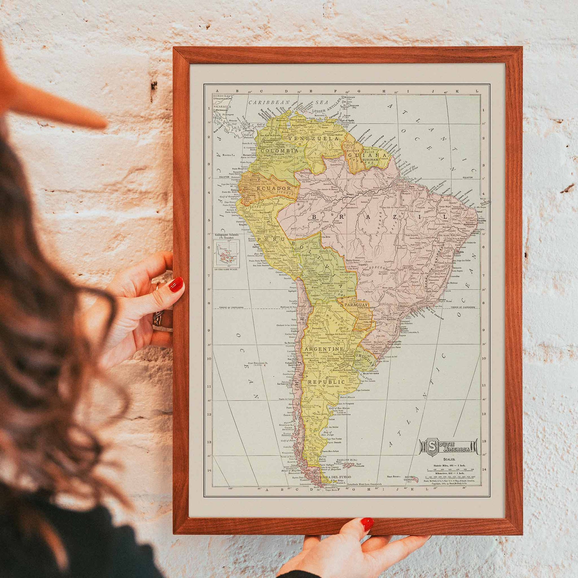 Vintage Rand McNally South America map poster with labeled continent in soft yellow pink and beige cartographic detail, framed and displayed in modern living room decor